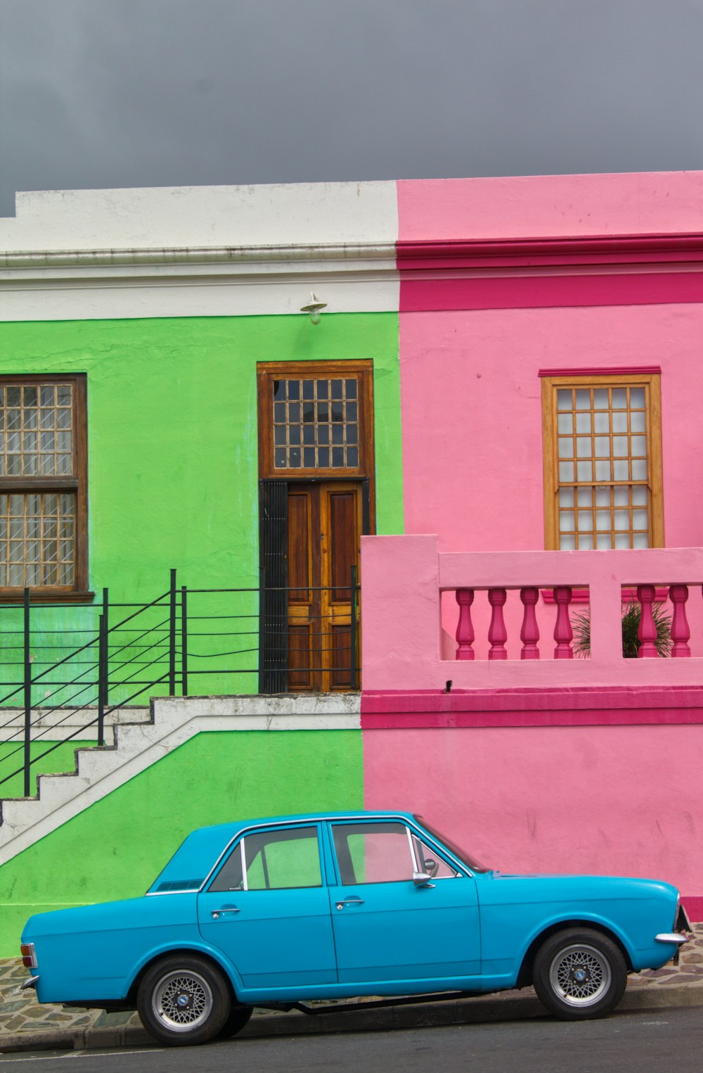 blue sedan parked beside pink and green house