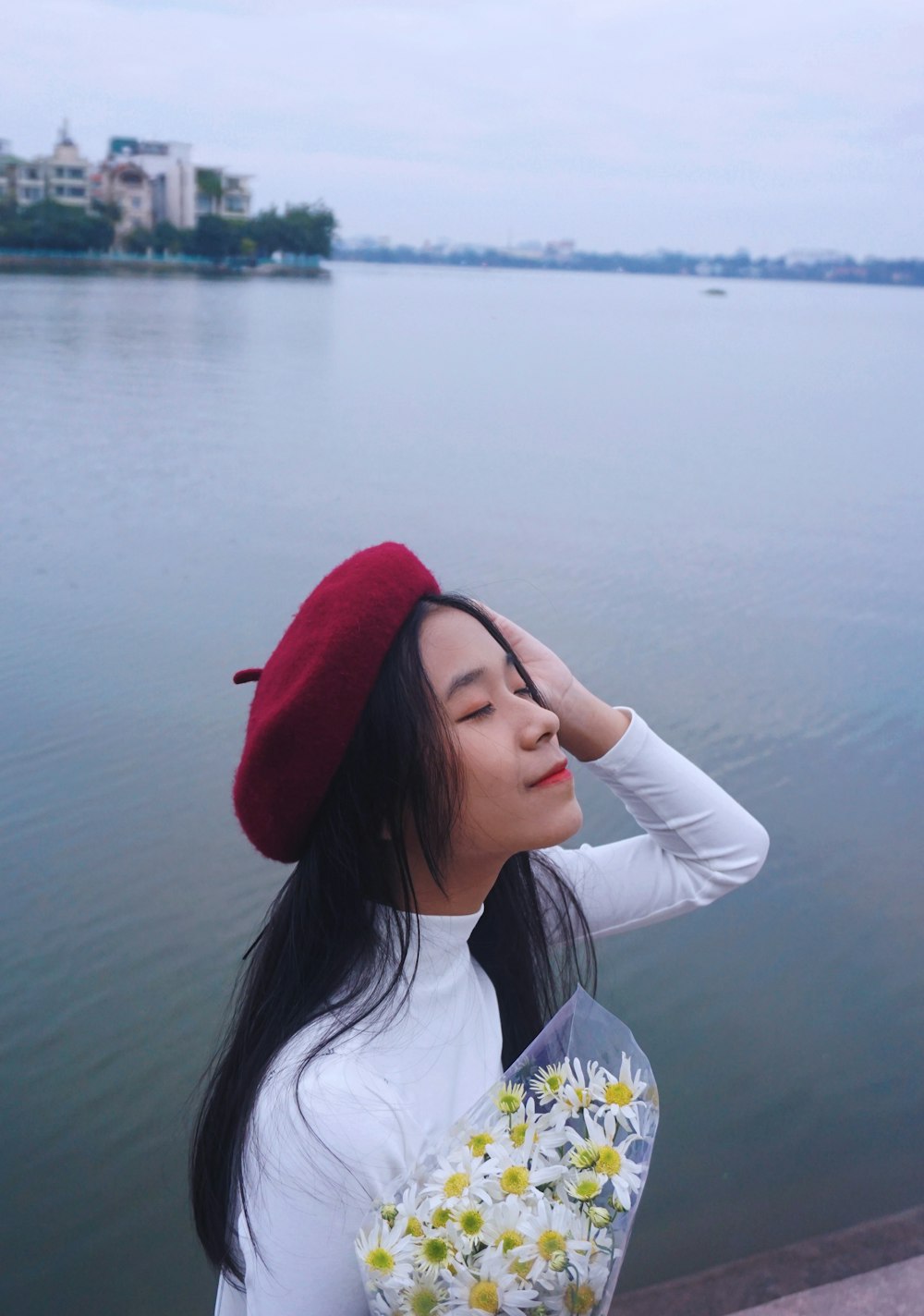 woman standing and touching hair using left hand near body of water