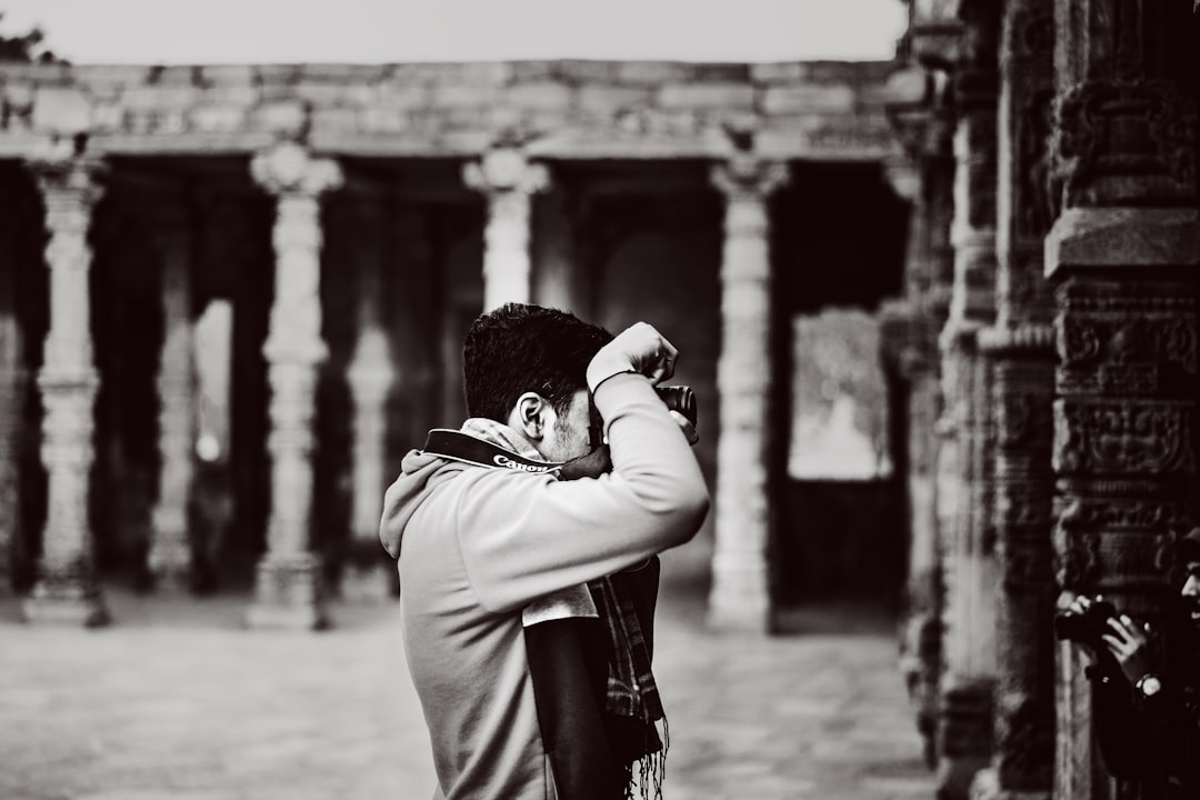 grayscale photography of man taking photo beside concrete wall
