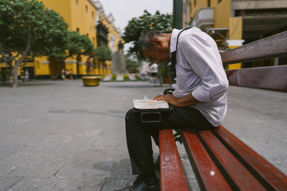 man sitting on brown bench near building