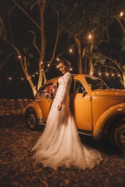 woman in white wedding dress standing beside yellow Volkswagen Beetle coupe