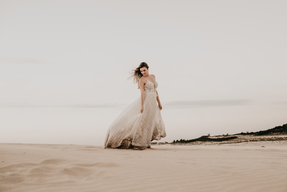 woman wearing white gown standing on sand during daytime