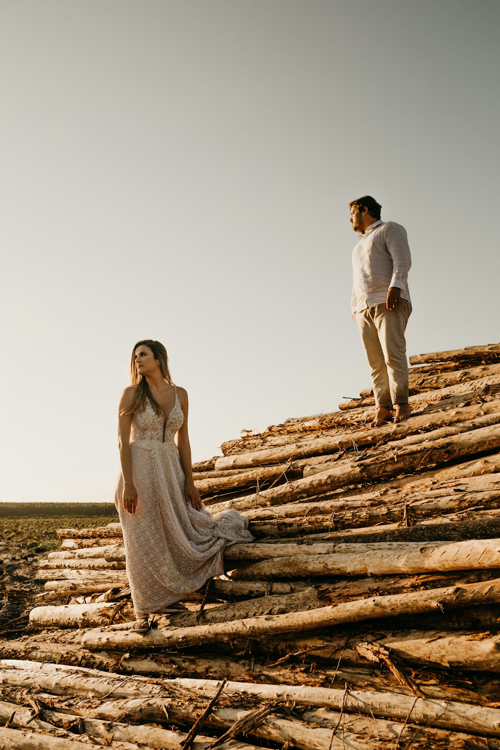 man and woman standing on pile of wood logs