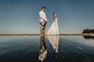 man and woman standing near calm body of water