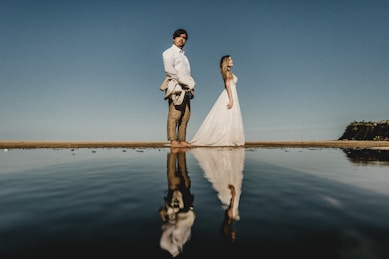 man and woman standing near calm body of water
