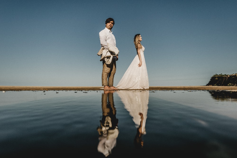 man and woman standing near calm body of water