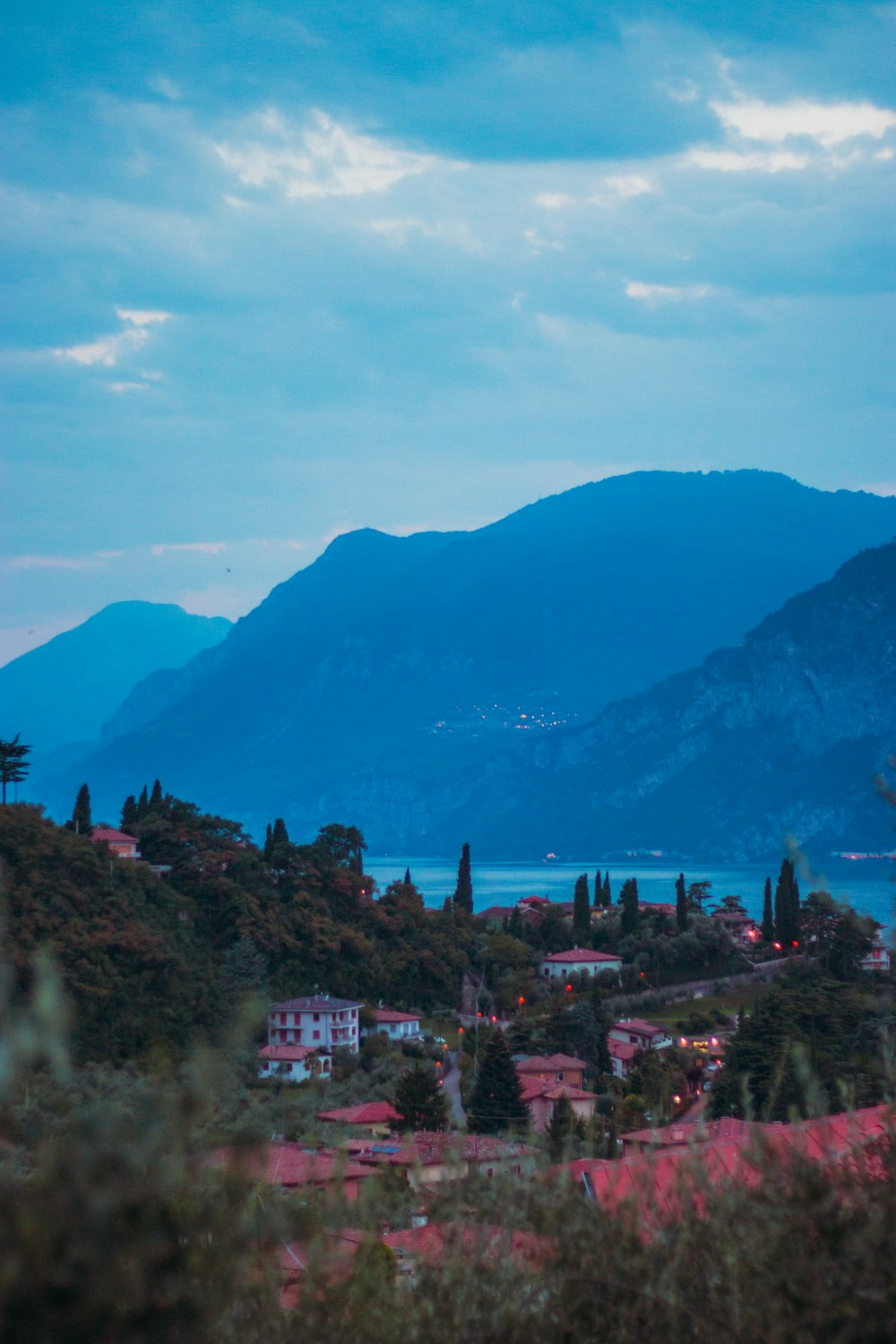 white and red buildings surrounded by trees near body of water with view of mountain under blue sky at daytime