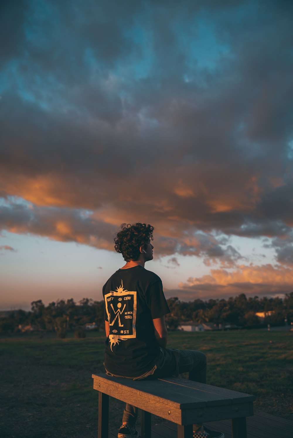 man sits on bench under dark sky