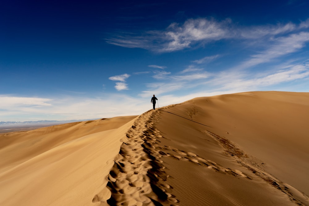 man waking on sand dune on desert under blue and white cloudy sky
