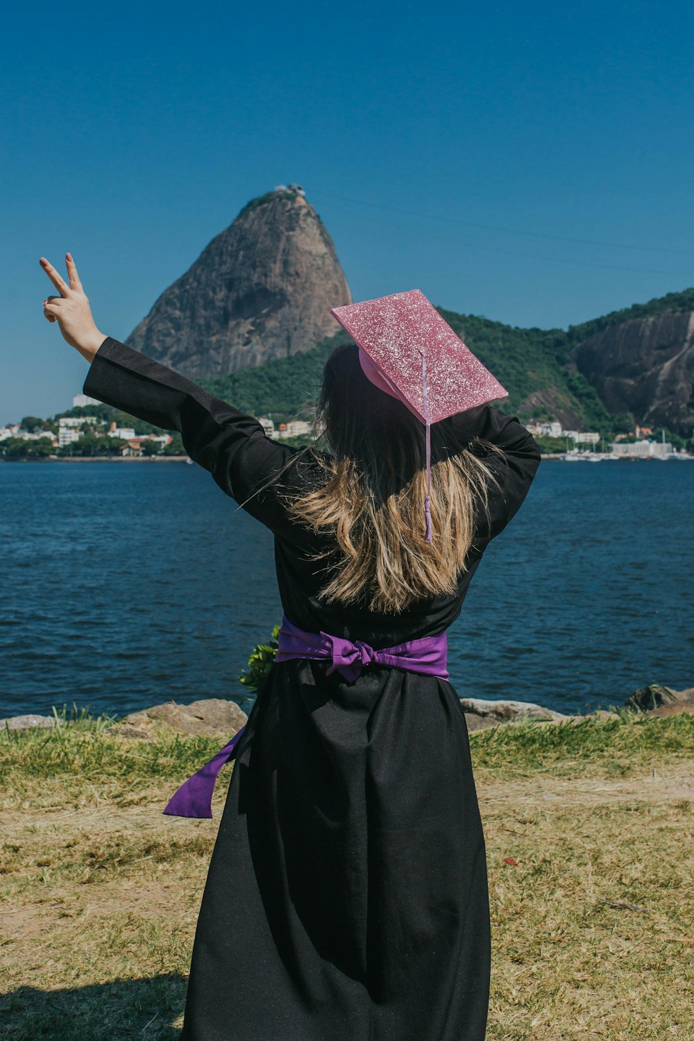 woman standing and making peace hand sign near body of water