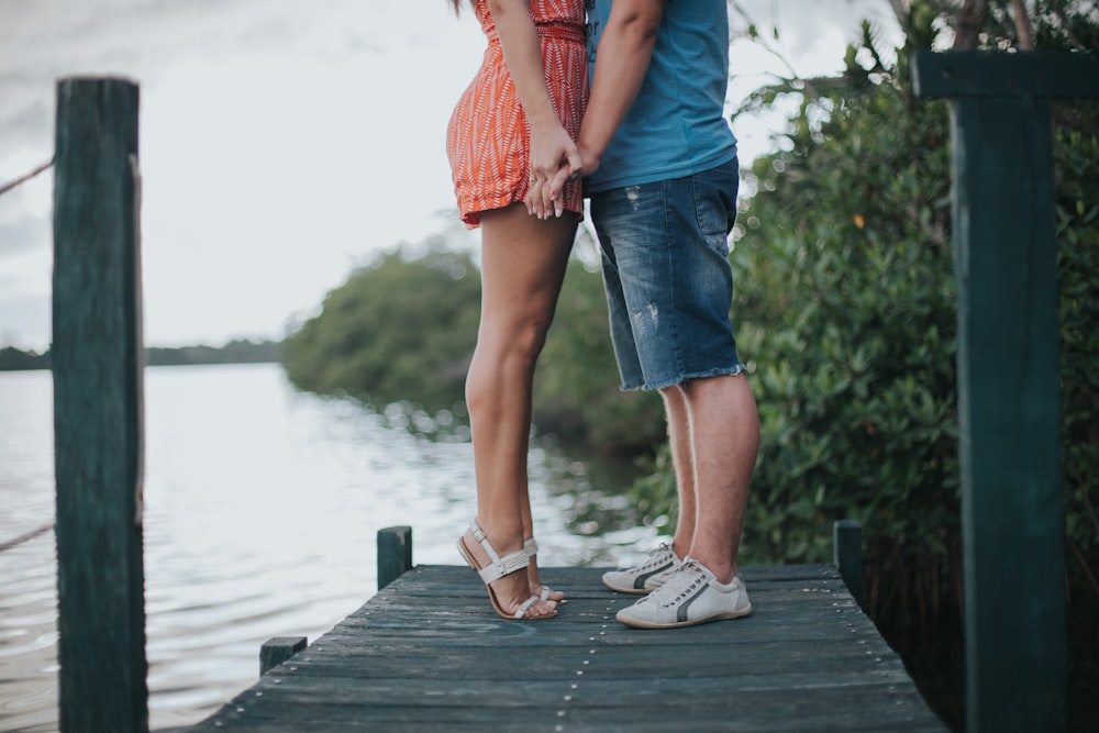 man and woman holding hands standing on gray wooden dock during daytime