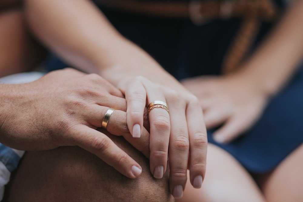 two hands with gold rings resting on knee