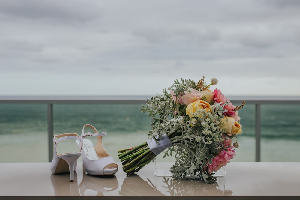 bouquet of flowers near white leather heeled sandals viewing calm body of water