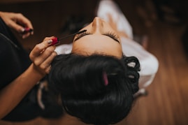 person putting mascara to a woman wearing white top