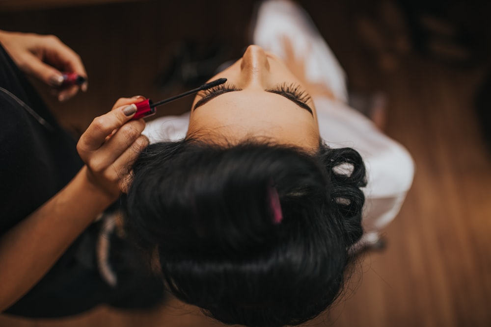 person putting mascara to a woman wearing white top