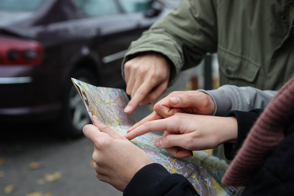 three person pointing on map near street during daytime