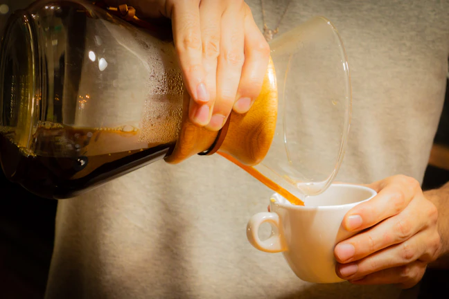 Artisan carefully pouring coffee from a golden pot into small cups, highlighting the ritual.