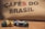 A collection of colorful coffee pods are scattered on a wooden surface in front of a burlap sack with the words 'CAFÉS DO BRASIL' printed on it.