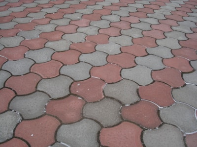 Interlocking concrete pavers form a repeating pattern on the ground, featuring alternating red and grayish-green colors.
