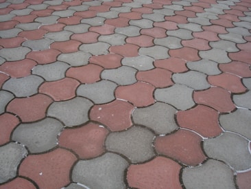 Interlocking concrete pavers form a repeating pattern on the ground, featuring alternating red and grayish-green colors.