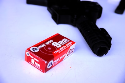 A box of 9mm full metal jacket ammunition clearly marked with 'THAI ARMS' is placed on a white surface. Next to the box is a firearm with a visible barrel and grip.