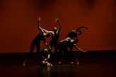 A group of dancers performing a synchronized contemporary routine on a dark stage