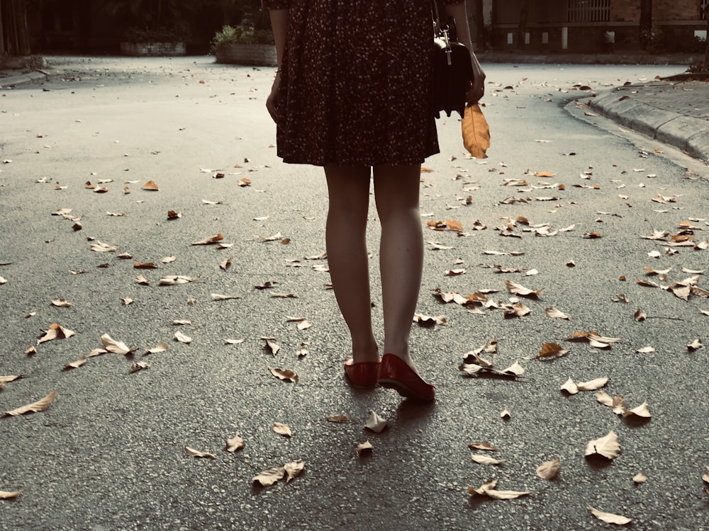 woman walking on concrete pavement with withered leaves