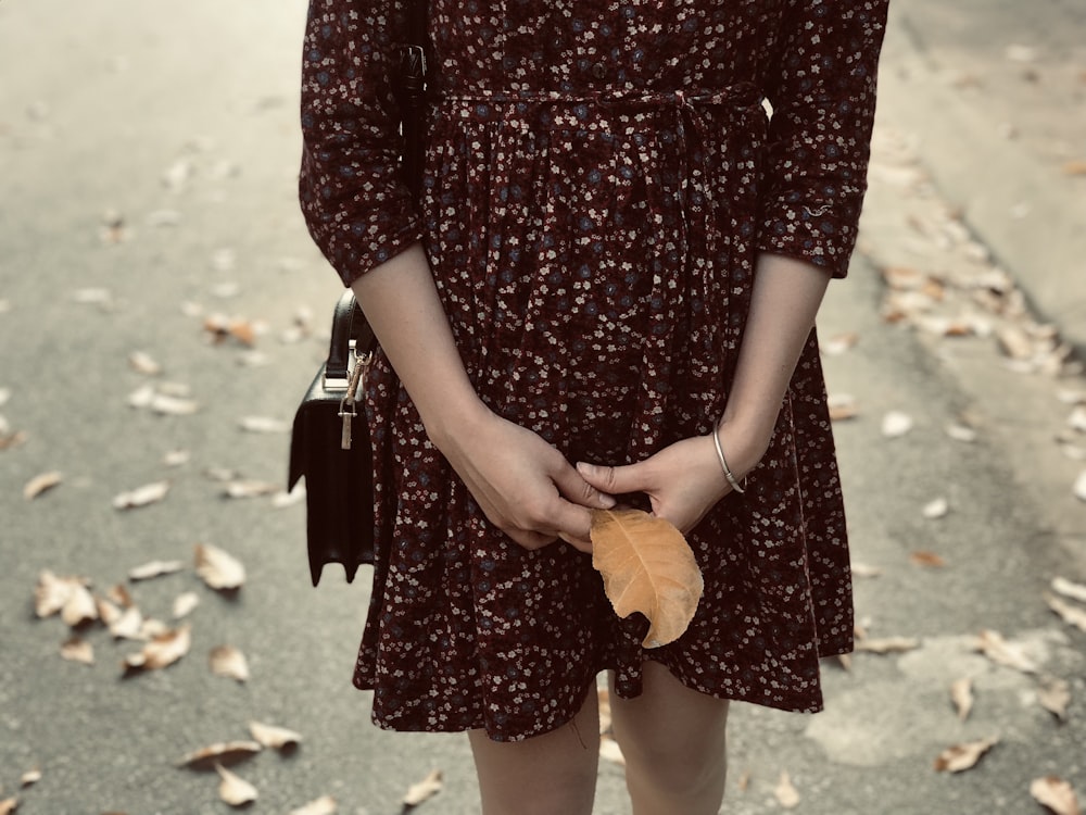 woman holding brown leaf standing on street