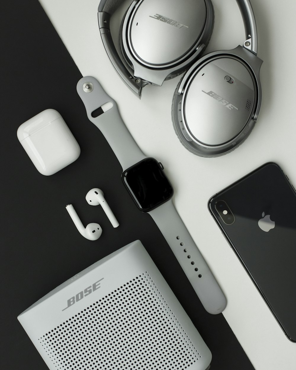 auriculares Bose grises, Apple Watch y iPhone sobre superficie blanca y negra