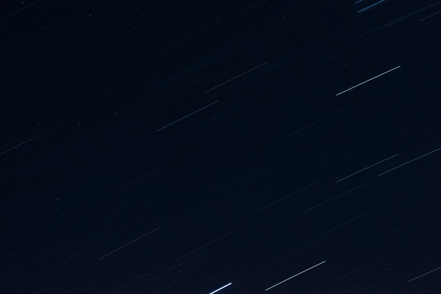 Long exposure photograph capturing star trails across a deep, dark night sky.