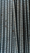 Close-up view of multiple parallel steel rebar rods with a textured, ribbed surface. The bars have a weathered and industrial appearance, indicating they are used in construction settings.