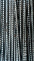 Close-up view of multiple parallel steel rebar rods with a textured, ribbed surface. The bars have a weathered and industrial appearance, indicating they are used in construction settings.
