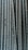 Close-up view of multiple parallel steel rebar rods with a textured, ribbed surface. The bars have a weathered and industrial appearance, indicating they are used in construction settings.