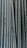 Close-up view of multiple parallel steel rebar rods with a textured, ribbed surface. The bars have a weathered and industrial appearance, indicating they are used in construction settings.