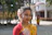 A cheerful young woman wearing a flowing ethnic dress from khushmita, walking along a colorful street market.