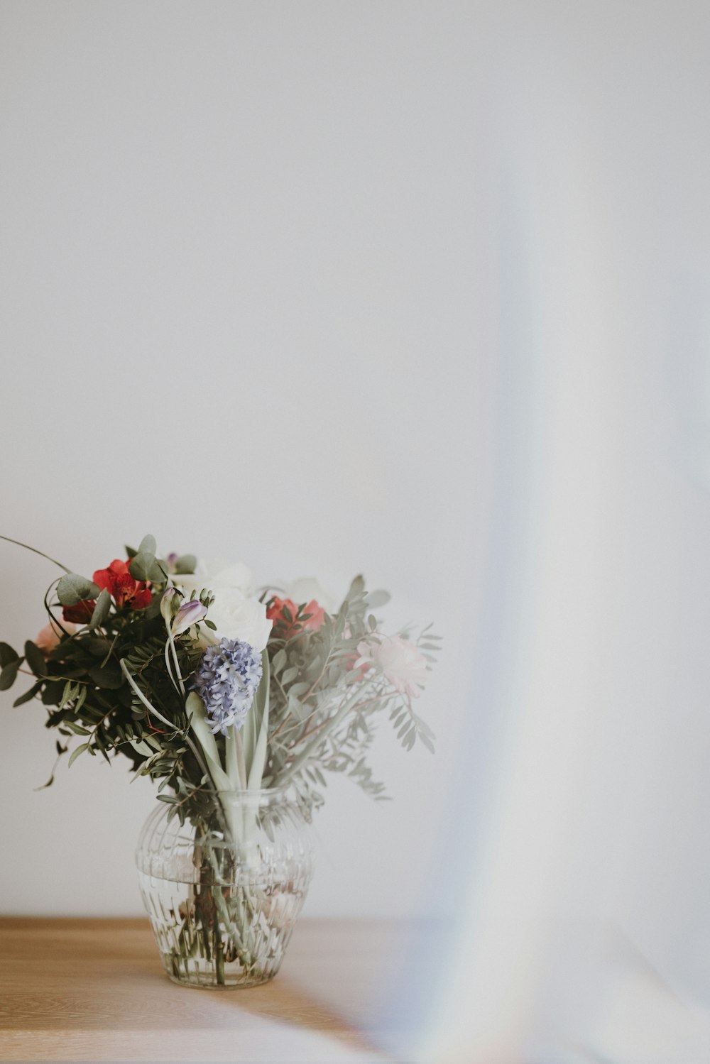 red flower on clear glass base near the white wall