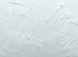 A textured white surface with various overlapping strokes and patterns giving a rough, plaster-like appearance.