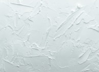 A textured white surface with various overlapping strokes and patterns giving a rough, plaster-like appearance.