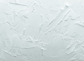 A textured white surface with various overlapping strokes and patterns giving a rough, plaster-like appearance.