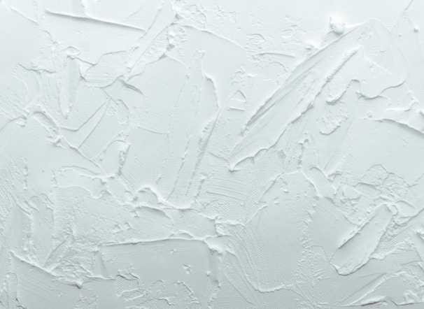 A textured white surface with various overlapping strokes and patterns giving a rough, plaster-like appearance.