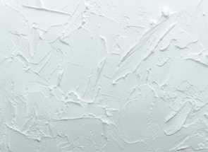 A textured white surface with various overlapping strokes and patterns giving a rough, plaster-like appearance.