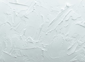 A textured white surface with various overlapping strokes and patterns giving a rough, plaster-like appearance.