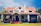 A charming house with a vintage design featuring a red tiled roof and white walls. The building has a symmetrical facade with a central entrance. The front porch is covered with vines and surrounded by a well-maintained lawn.