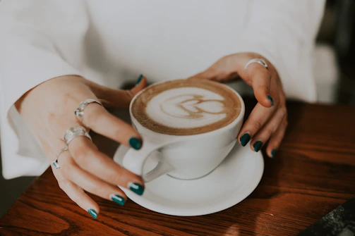 Hands gently holding a coffee cup, showcasing glossy cream and mocha nails with a refined editorial vibe.