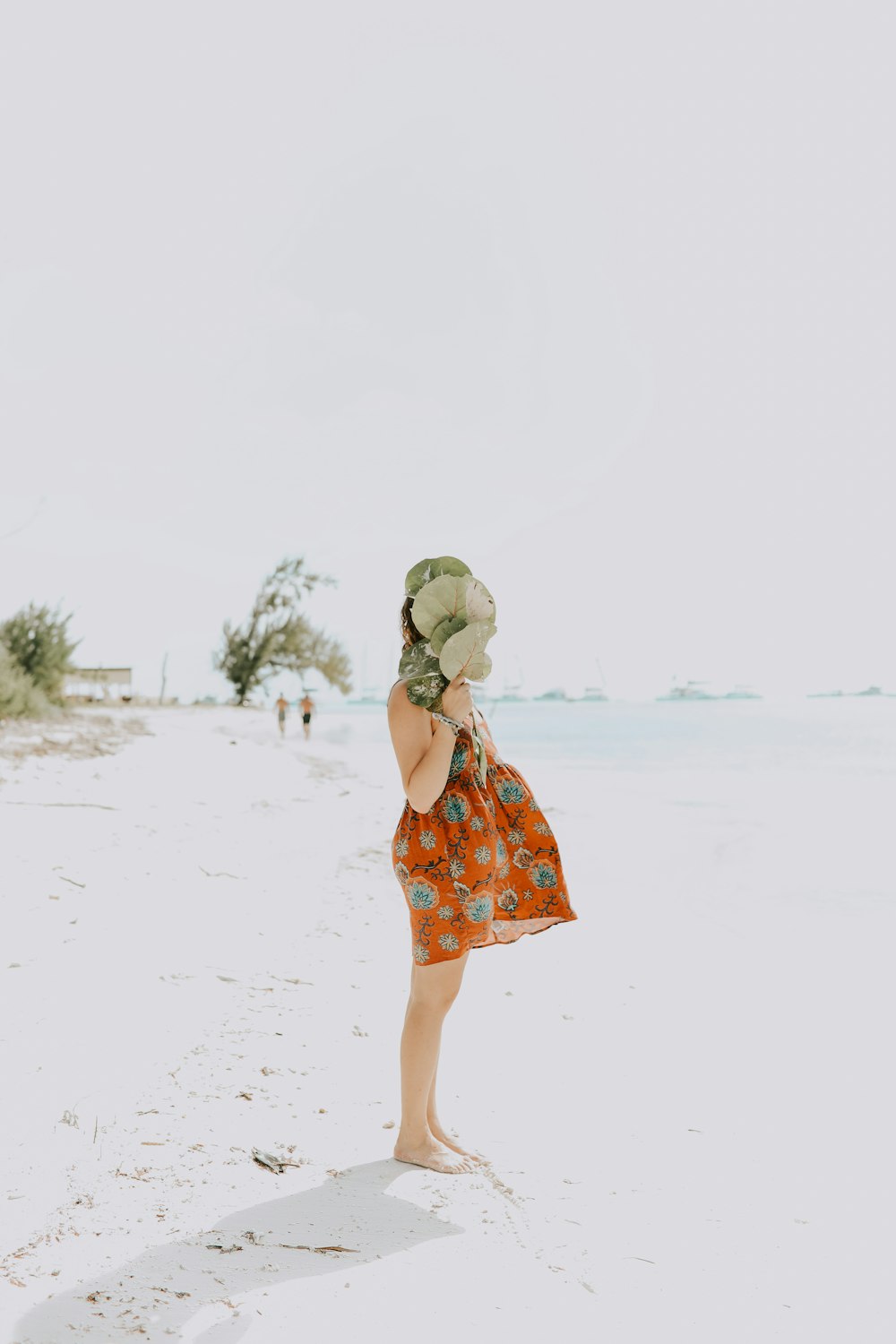 昼間、ベージュの砂の上に立つオレンジと緑の花柄のドレスを着た女の子