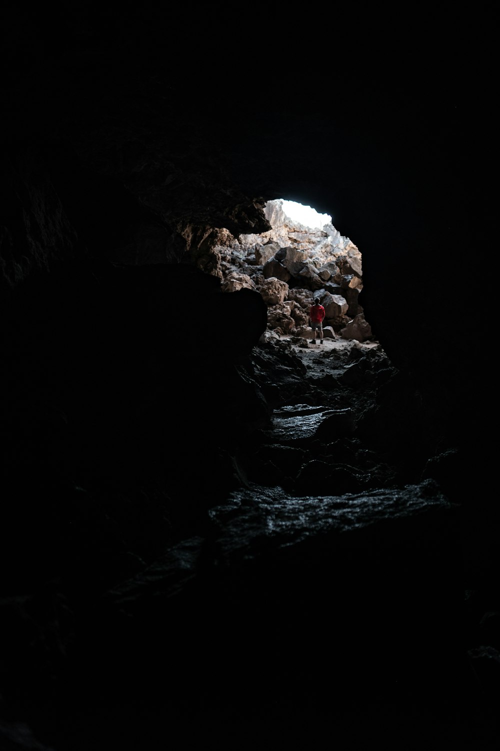 a person standing in a dark cave with a light at the end