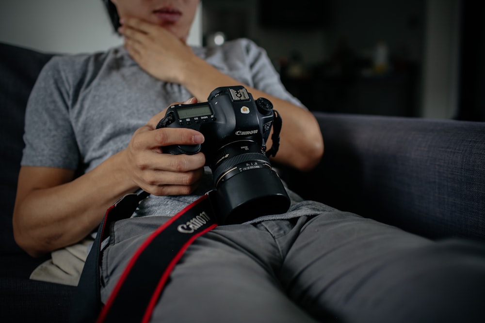 person sitting on gray sofa watching on black Canon DSLR camera