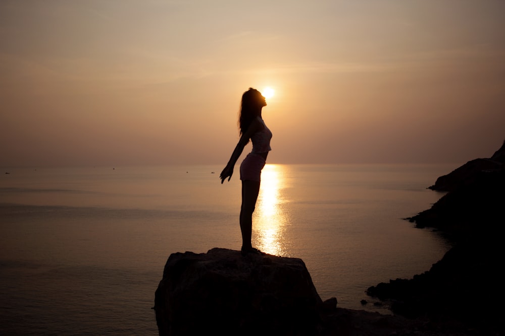 silhouette of woman standing on sea cliff during golden hour