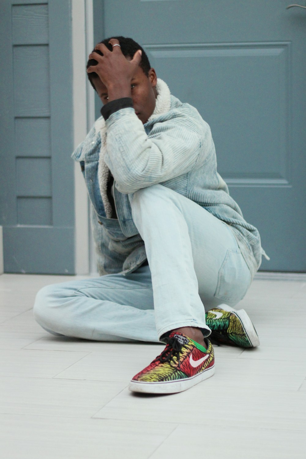 man wearing blue jacket sitting on floor with left hand on head