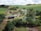 An aerial view of a rural landscape featuring a farmhouse surrounded by lush greenery and multiple small ponds. The property includes solar panels on the building roofs, and is set amidst rolling fields and scattered trees. The sky is overcast with clouds, adding depth to the scenery.